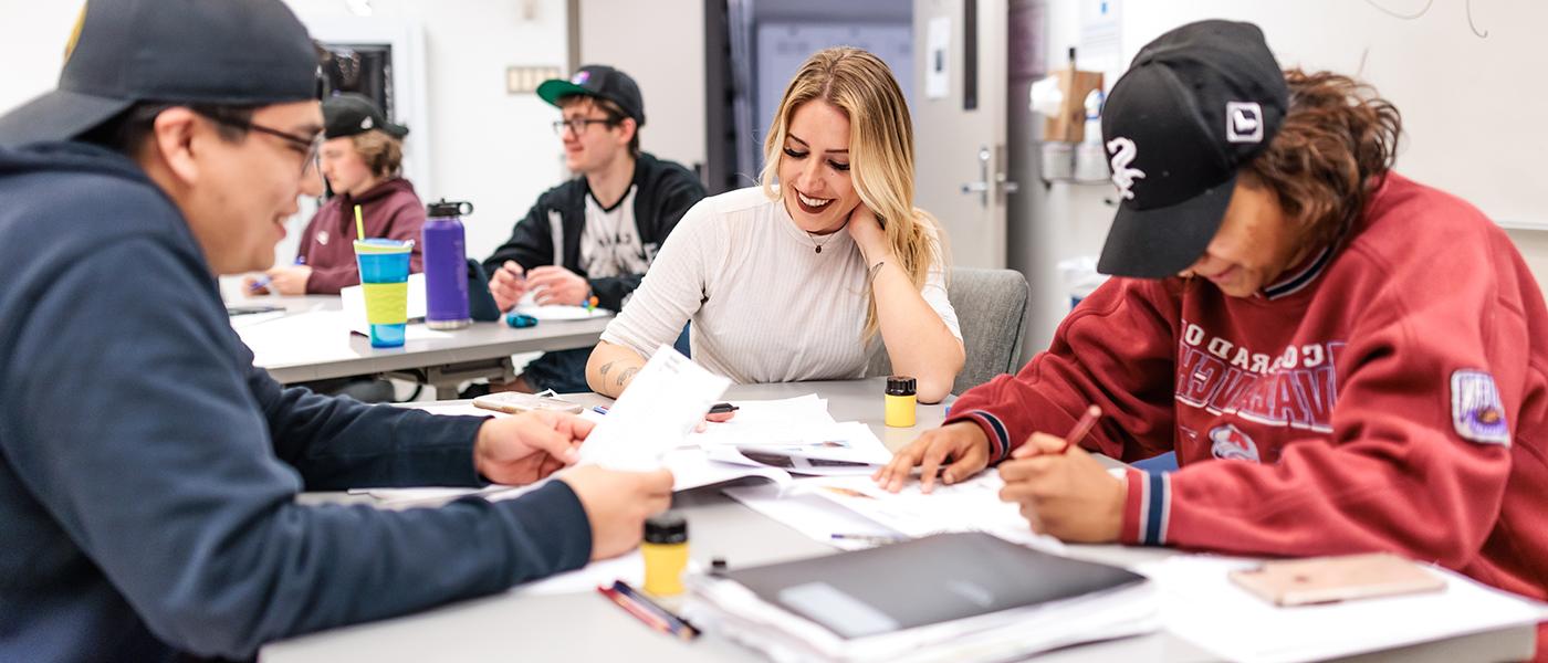 Three students sit at a table working together in a group, smiling at one another.